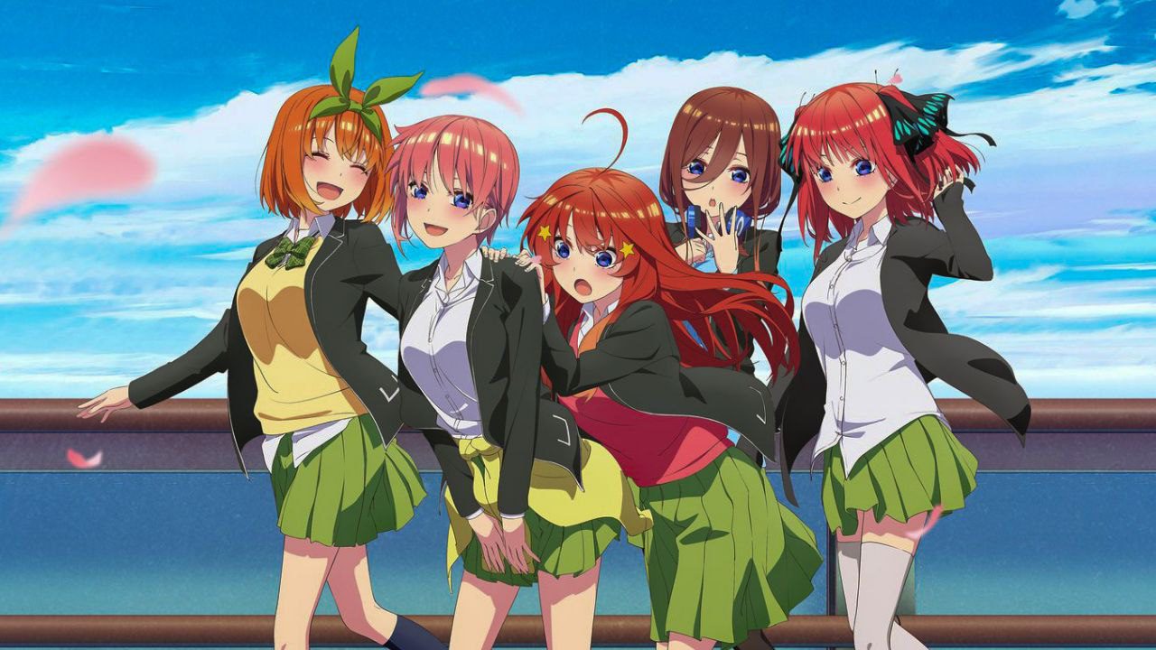 The five Nakano sisters from The Quintessential Quintuplets standing together in school uniforms by the seaside.