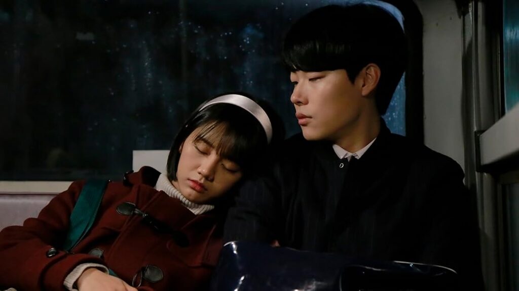 A young girl sleeping on a boy’s shoulder while sitting together on a bus at night in Reply 1988.